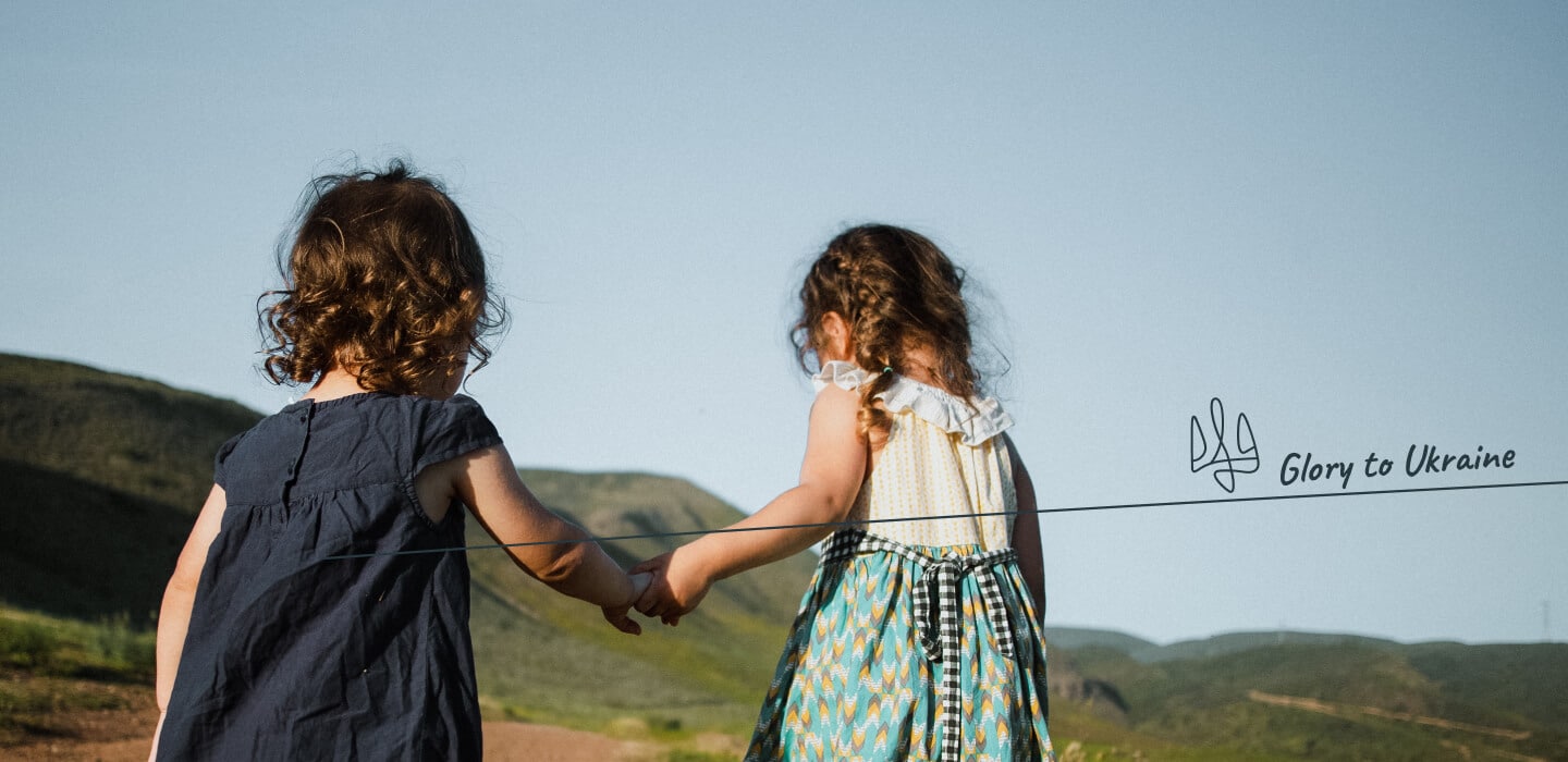 Two kids, hand in hand, are watching the mountains. Tryzub, or trident, symbolizing sovereignty, resilience, and connection to generations.